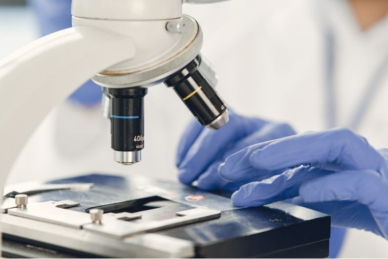 Hands in blue gloves setting a slide under a microscope