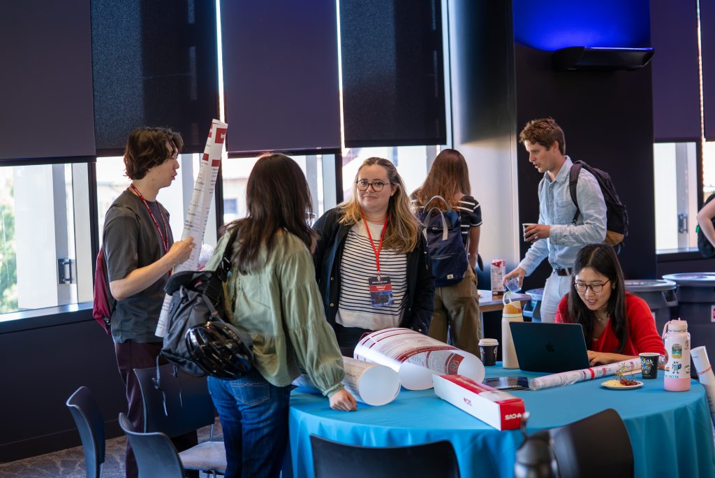 Rebecca Hurwitz (center) and other students converse at a table before poster presentations.