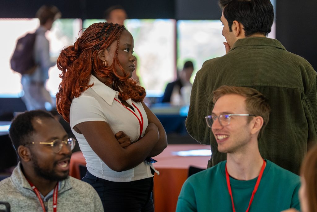 Ishaq Balogun and Peter Neidlinger talk in the foreground. Ashley Tamdjo stands behind them.
